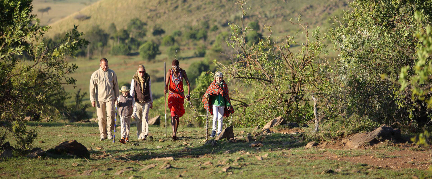 Family walking through a jungle during foot safari. Understand the differences between a Kenya vs Tanzania Safari